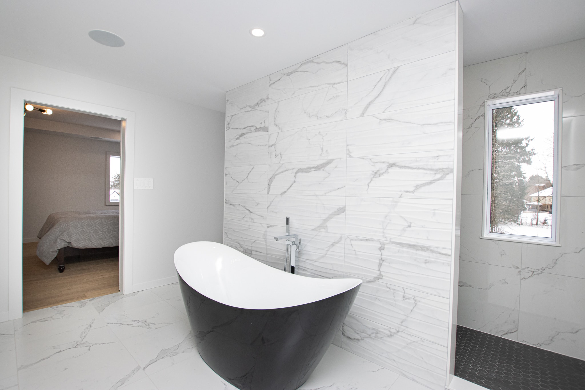Master ensuite with freestanding black tub and marble tile